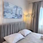 Monte Vista Lemnos Apartments bedroom with a grey upholstered headboard, sailboat artwork, soft curtains, and warm pendant lighting beside the window.