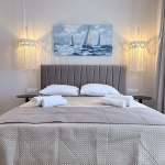 A softly lit Monte Vista Lemnos Apartments bedroom with a gray upholstered bed, sailboat painting, bedside tables, and woven pendant lights.