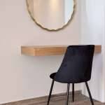 Elegant Monte Vista interior corner with a gold-framed round mirror, floating wooden shelf, and black velvet accent chair on wood-look flooring.